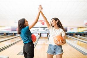 two teenagers high-fiving after bowling throw