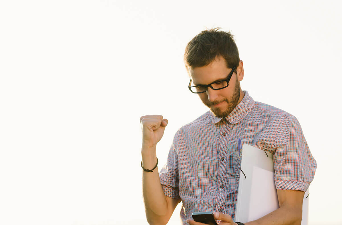 businessman happy with his fist in the air while looking at his phone